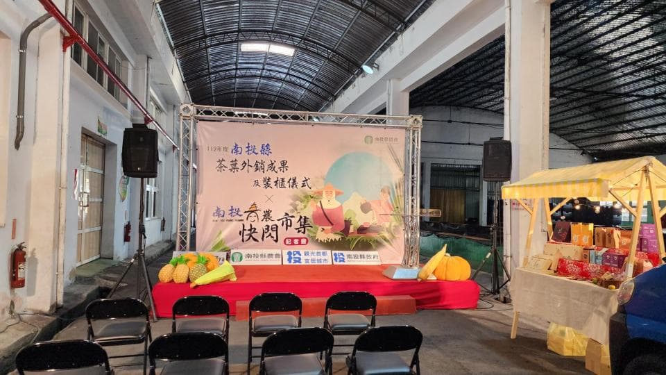 這張照片是一個室內的活動場地,最重要的是一個舞臺,舞臺上有一個大型的廣告看板,上面寫著活動的標題和贊助商信息,舞臺前面擺放了一些椅子,似乎正在等待活動開始。