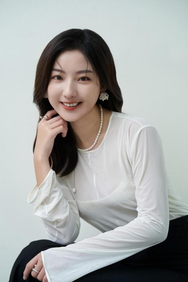 這張照片是一個年輕女性的半身照,她穿著白色襯衫,笑著看著鏡頭,她的笑容和溫暖的眼神是最吸引人的地方。