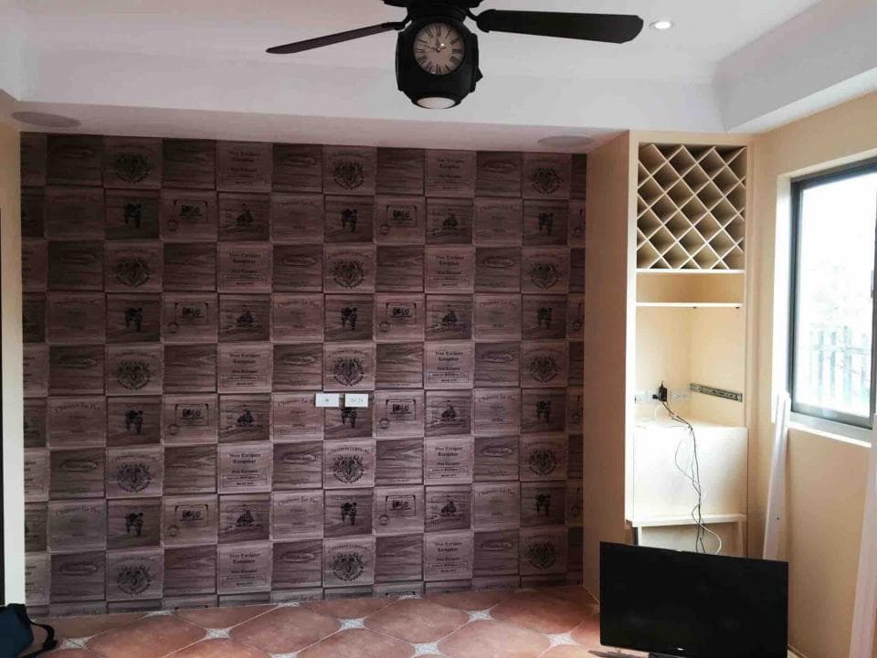 1) 照片顯示一個帶有木箱圖案的牆壁、一台吊扇、一個木質酒架、一個電視和一個部分可見的窗戶