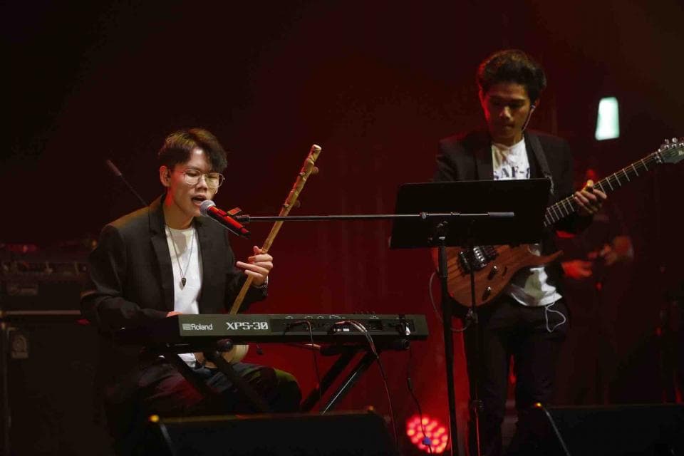 這張照片是一個音樂表演的現場,最重要的是舞臺上正在表演的歌手,他正在演奏電子琴並演唱歌曲,他的神情專注,動作充滿力量。