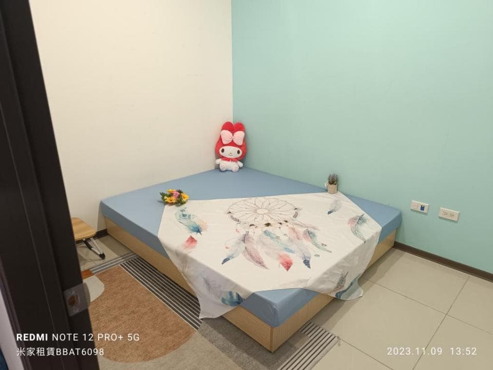 1) 照片中顯示一個房間,房間裡有一張床,床上的床單上有羽毛和捕夢網的圖案,床邊有一個小凳子,牆壁上有粉紅色的毛絨玩具