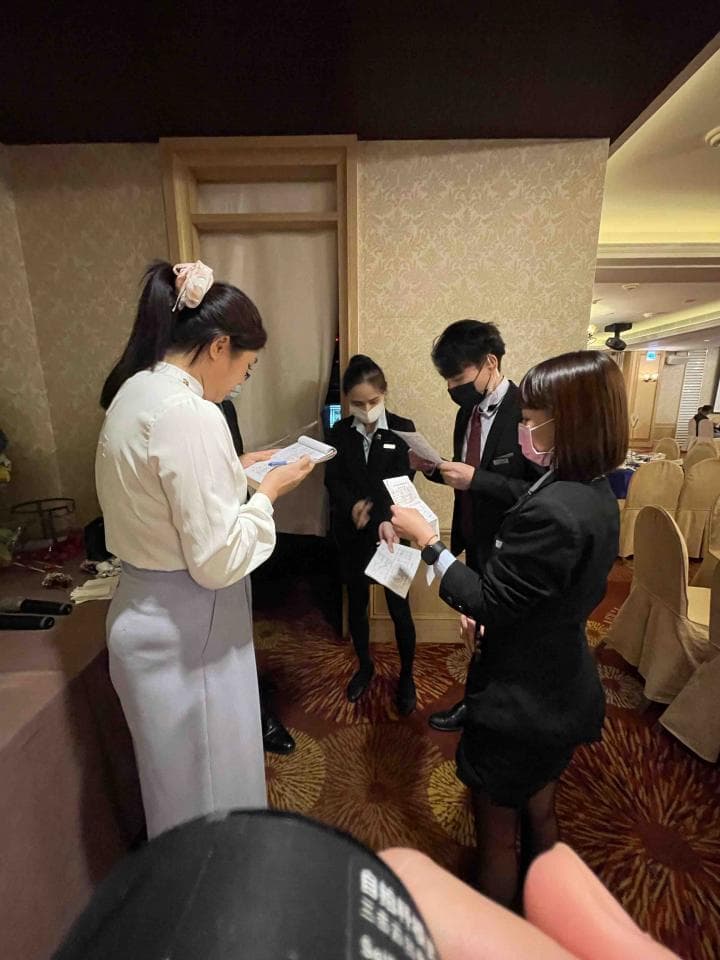 這張照片是四位身穿制服的人在一個酒店大廳,其中兩位穿著黑色西裝,另外兩位穿著白色襯衫和黑色裙子。他們看起來是在辦理登記手續或進行一些工作。