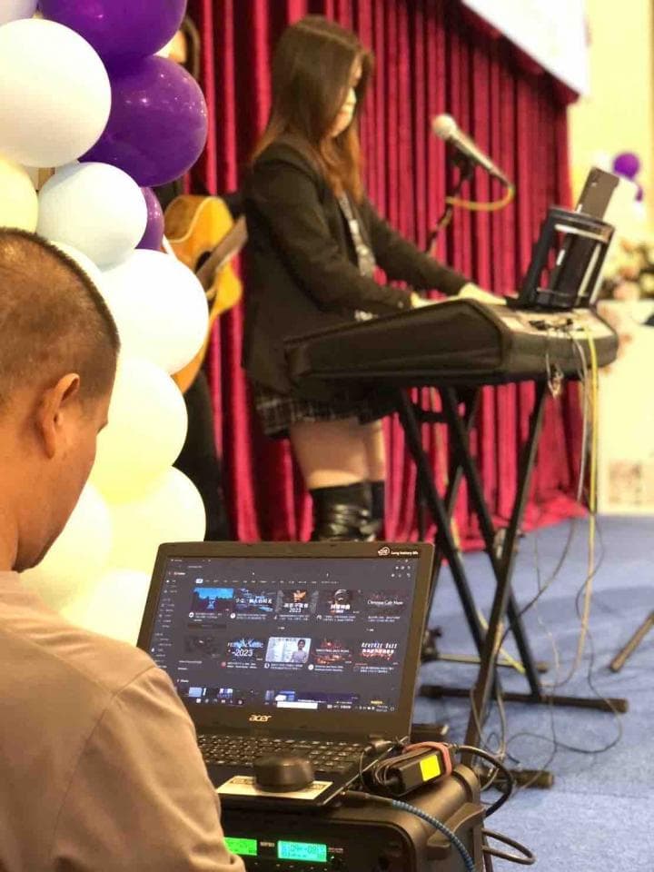 這張「音樂表演」的照片是一個女子在舞台上演奏鍵盤,旁邊有一位觀眾正在用電腦錄影。