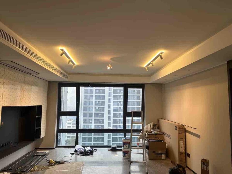 1) 這是一張室內照片,顯示一個客廳,牆上有一台電視,一個大窗戶,房間裡有一個梯子,一些箱子和一盞燈