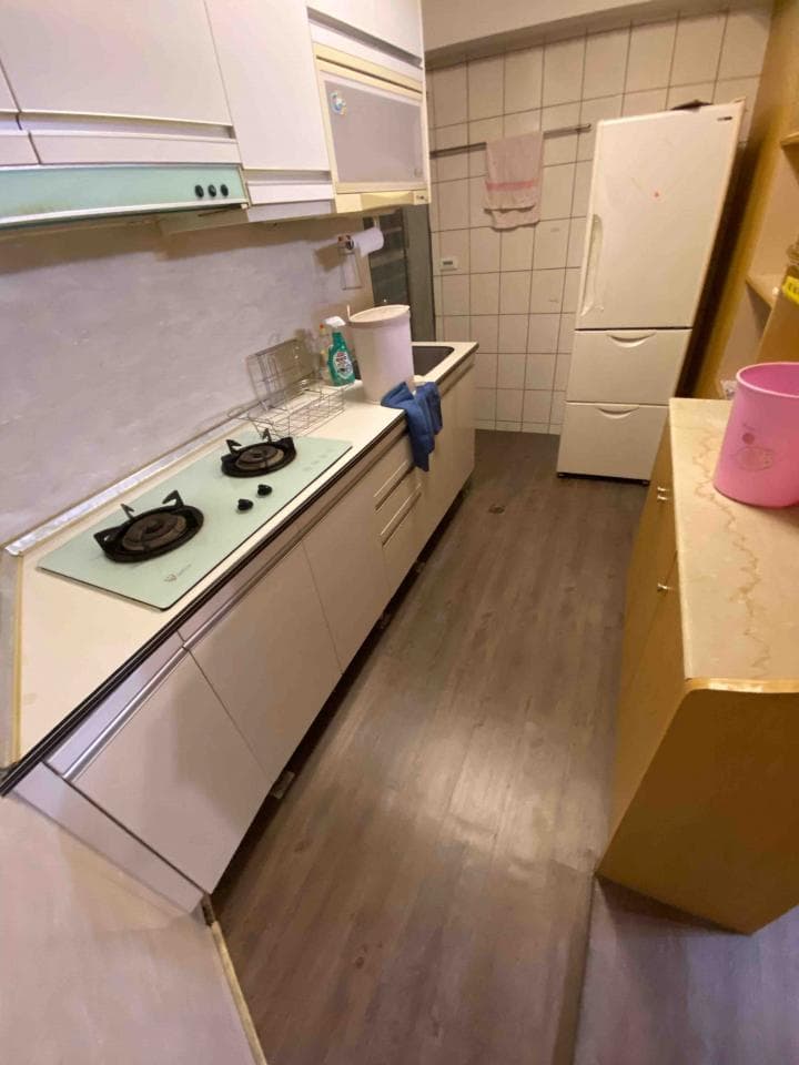 1) 照片顯示一個廚房,廚房裡有一個白色流理台,流理台上有瓦斯爐,流理台旁邊有白色的櫥櫃,櫥櫃旁邊有一個冰箱,地板是木紋地板
