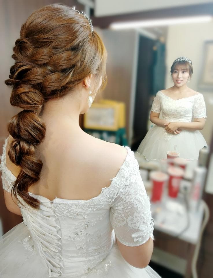 這張照片是一個女人穿著白色婚紗,她正在照鏡子。她的頭髮被編成了一個精緻的髮型,看起來很美麗。