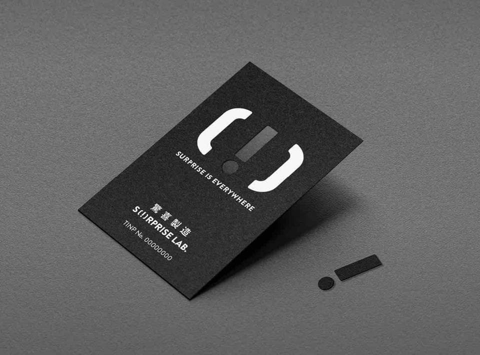 這張「商標」的照片是一個黑色卡片,上面有一個白色的驚嘆號和括號。卡片上寫著「驚喜製造 Surprise Lab」和「SURPRISE IS EVERYWHERE」。
