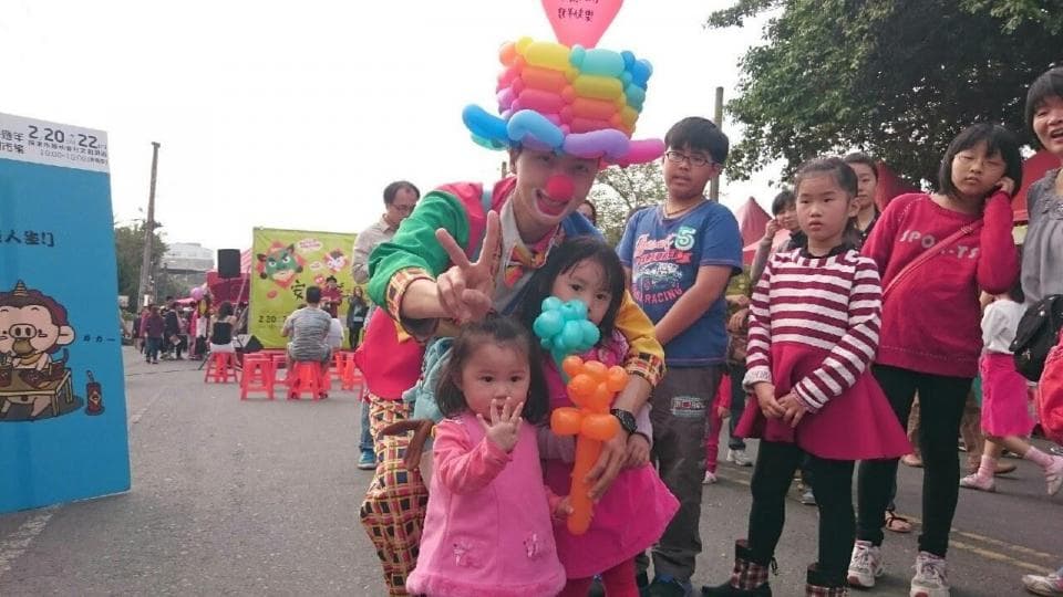 這張「街頭表演」的照片是一個穿著小丑服裝的表演者,他正在用氣球動物逗樂一群小孩。