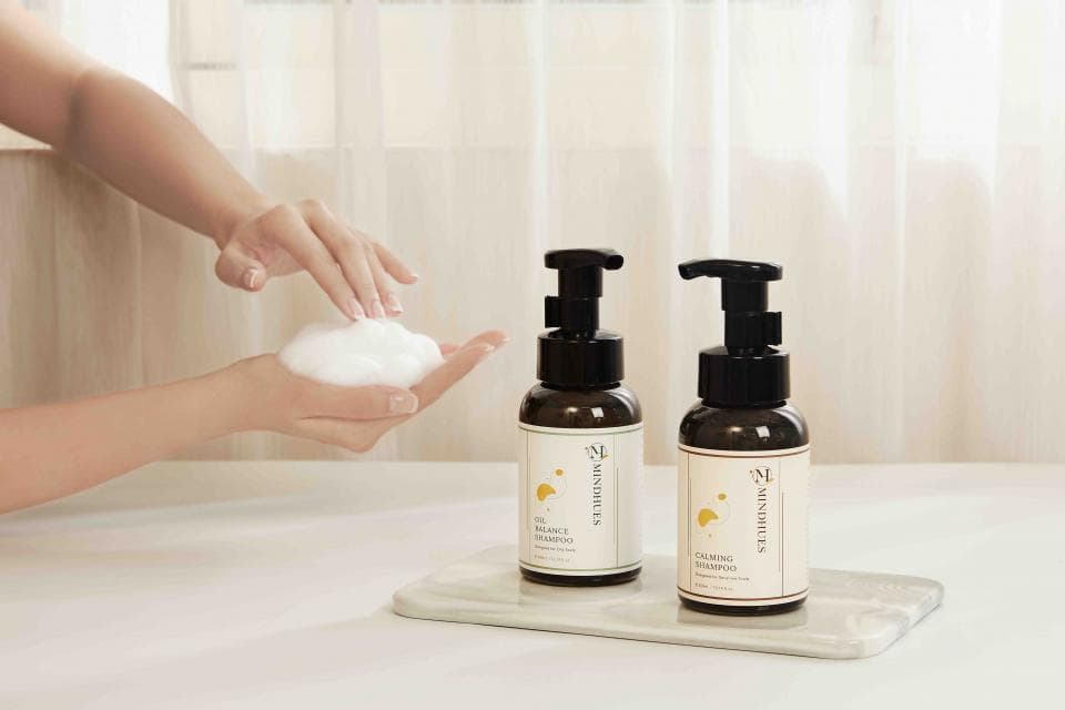 這張照片是 一個女人的手裡拿著一團泡沫,旁邊是兩瓶洗髮精。