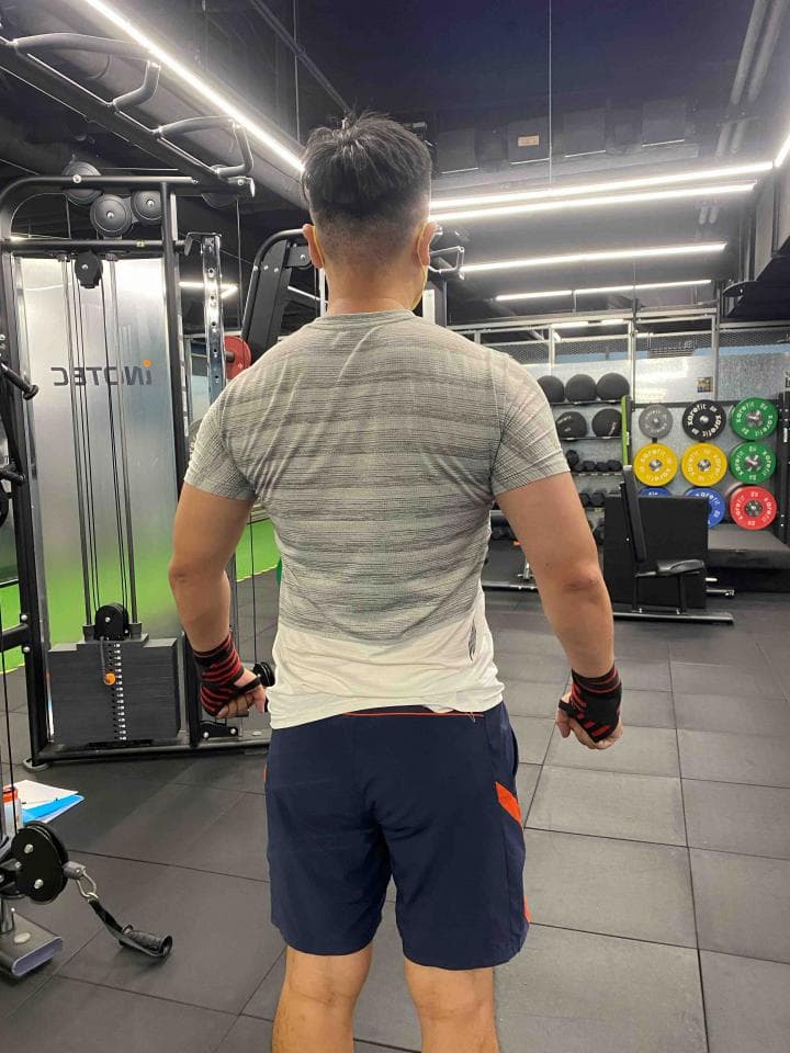 這張照片是一個健身房裡,一位穿著灰色T恤和藍色短褲的男子。他正在使用健身器材,並且戴著黑色的手套。