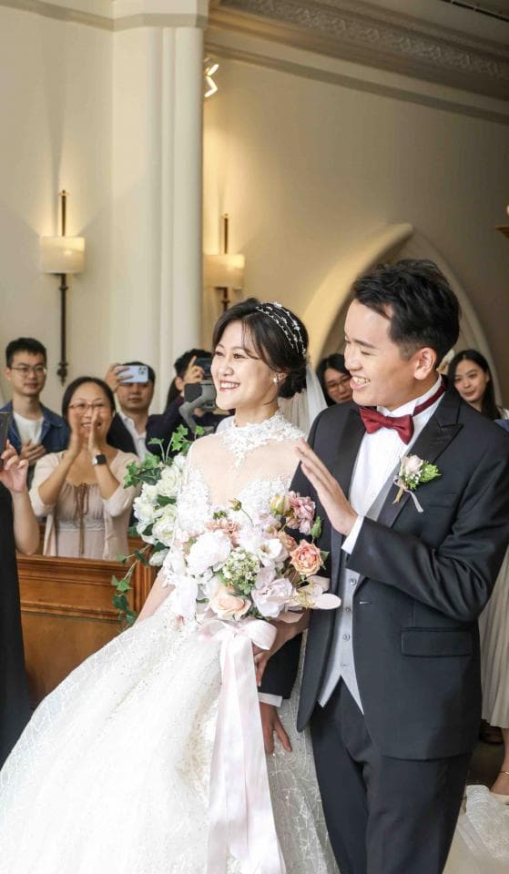 這張照片是一對新人正在教堂舉行婚禮。新娘穿著白色婚紗,新郎則穿著黑色西裝,他們手牽著手,正準備步入教堂。