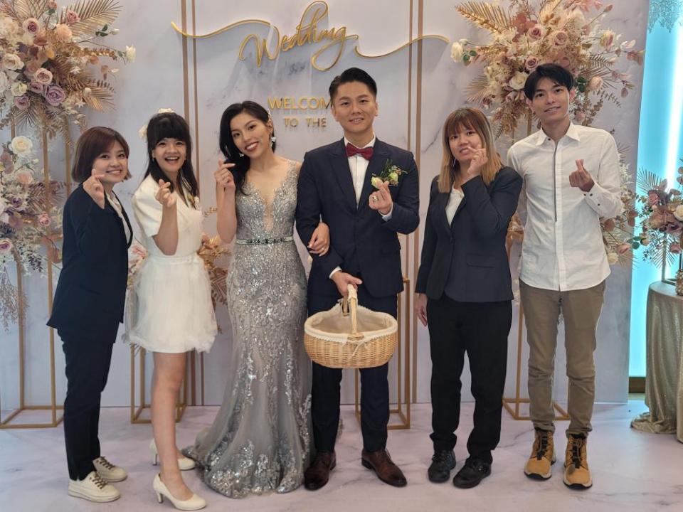 這張婚禮照片是新郎新娘和兩位伴娘及一位伴郎站在花牆前,新人笑容滿面,伴娘們也十分開心。