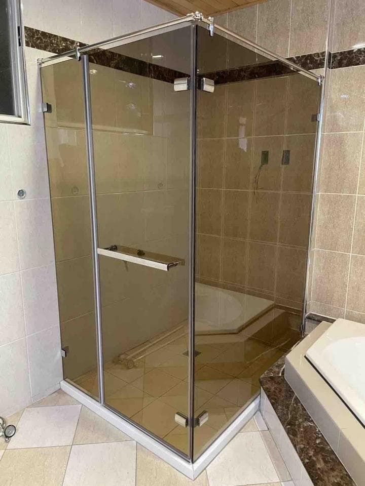 這張照片是一個現代化的浴室,重點是角落的玻璃淋浴間,它有三個玻璃面板,一個銀色的把手和一個白色的底座。