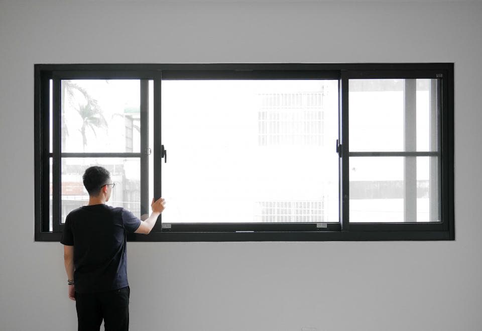 這張照片是一個男人站在窗戶旁,他正打開窗戶,讓陽光照射進來。