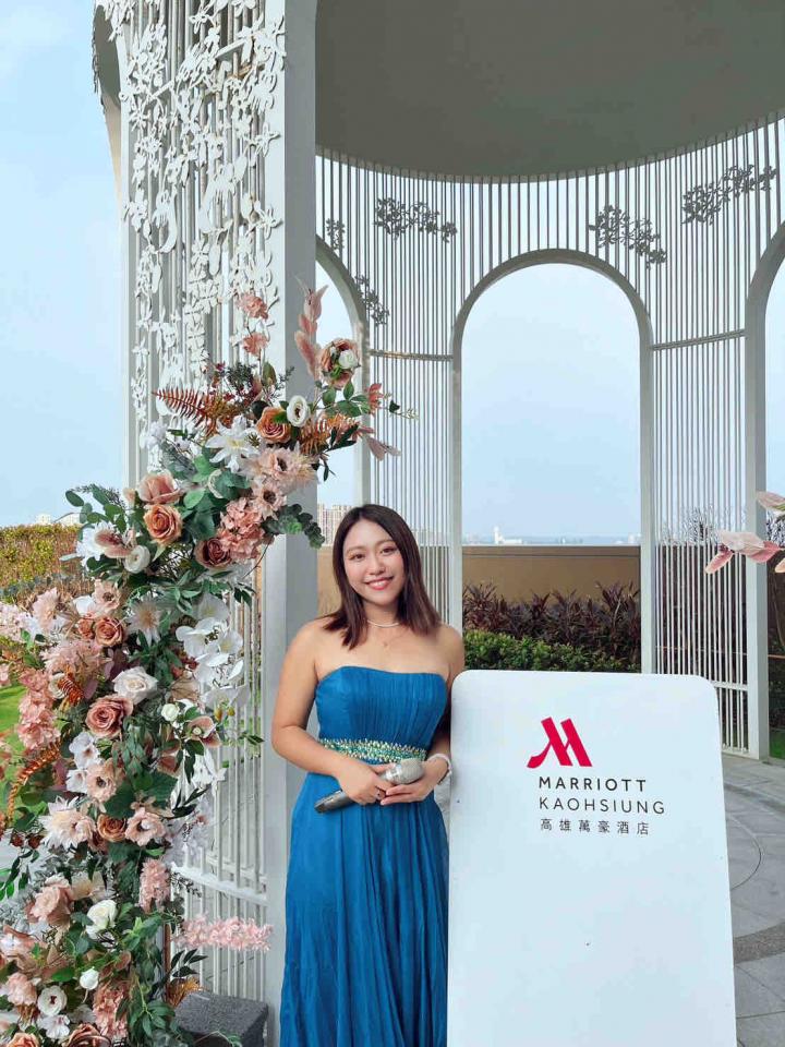 這張「婚禮場景」的照片是一對新人站在白色拱門前,新娘穿著藍色的禮服,新郎則穿著西裝。背景是綠色的草地和藍色的天空,還有許多花朵裝飾。