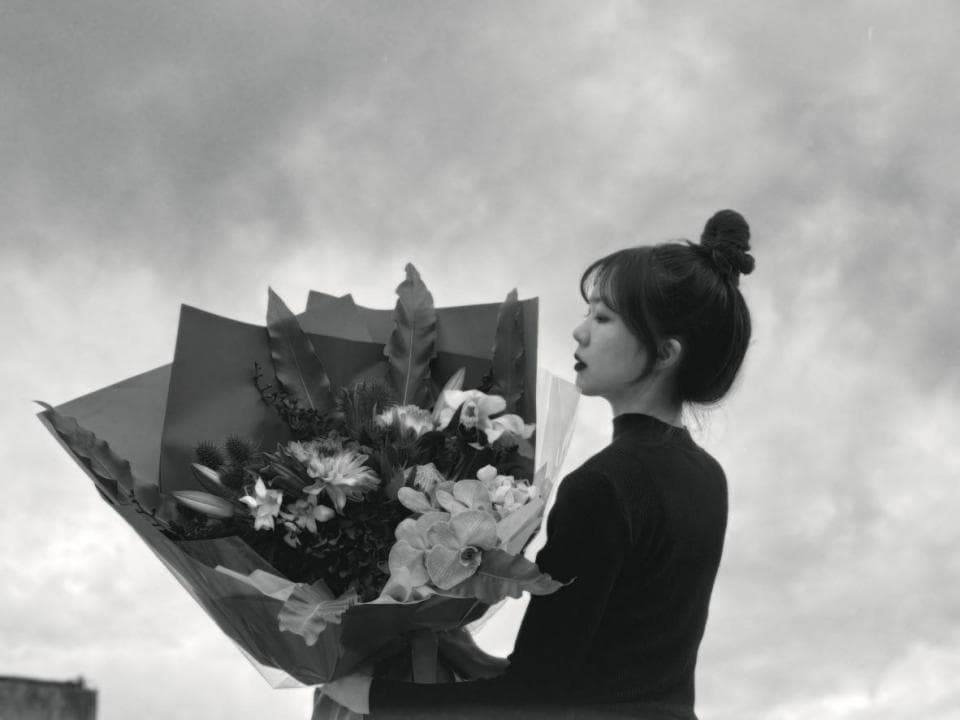 這張照片是一個年輕女子拿著一束鮮花,她穿著一件黑色的衣服,看起來很優雅。