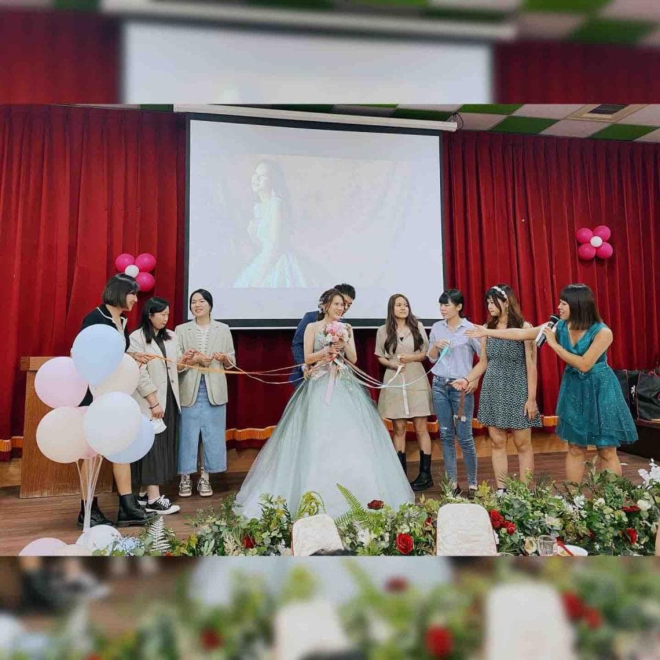 這張照片是一個婚禮現場,最重要的是新娘穿著一件藍綠色的婚紗,她站在舞臺上,旁邊有伴娘和朋友圍繞著她。