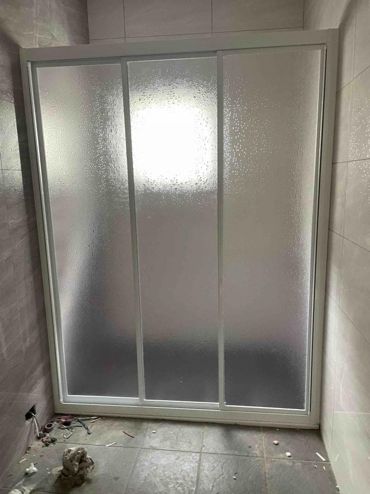 這張照片是一個浴室淋浴間的玻璃門。玻璃門是白色的,有三個部分,中間部分可以滑動。玻璃是磨砂的,可以保護隱私。