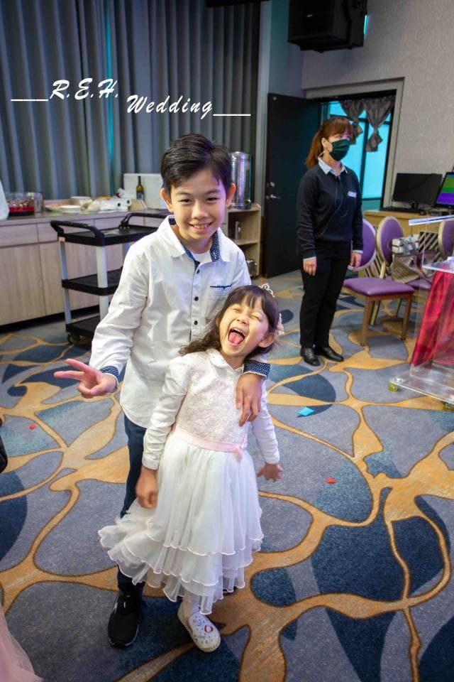 這張「婚禮」的照片是兩個小孩,一個男孩穿著白襯衫,一個女孩穿著白洋裝,站在地毯上,他們看起來很開心。