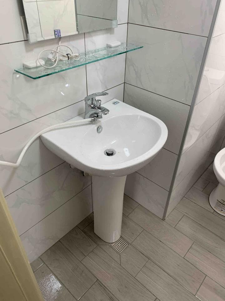 這張照片是一個浴室,主要部分是洗手台。洗手台是白色陶瓷製成的,有圓形台面和柱狀底座,台上裝有銀色的水龍頭,看起來乾淨整潔。