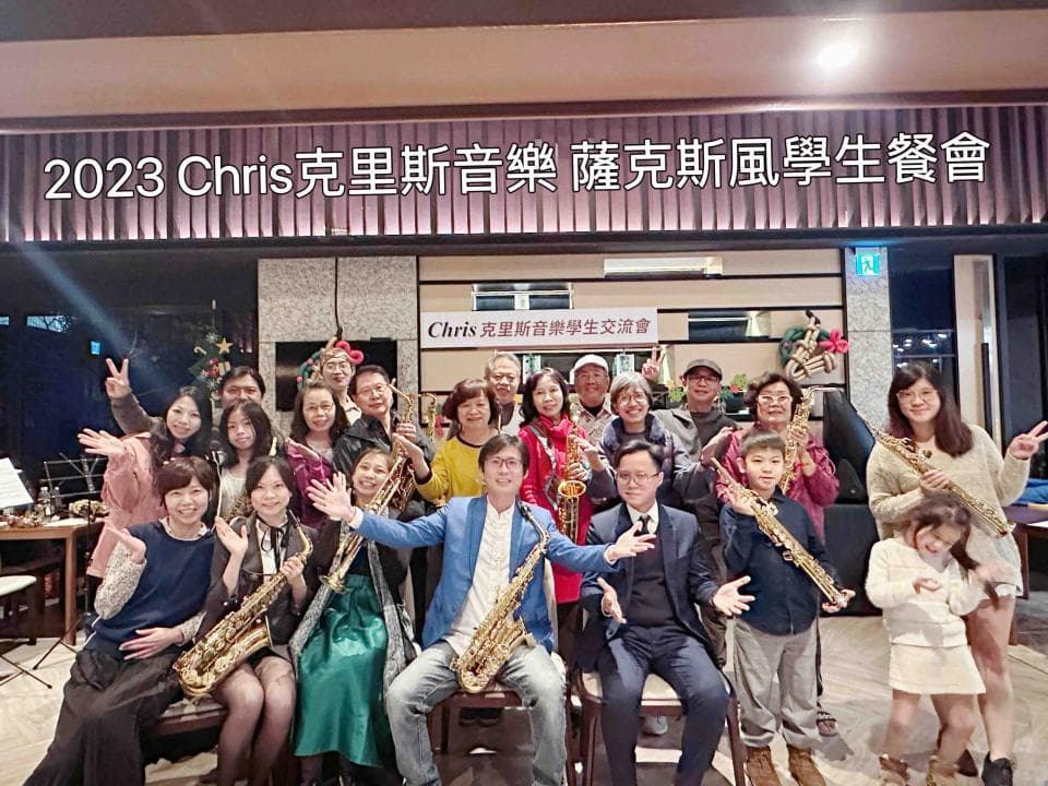 這張照片是一群學生在音樂教室表演,他們拿著薩克斯風,準備合奏,背景有「2023 Chris 克里斯音樂教室 演奏班風學生成績」的標語。