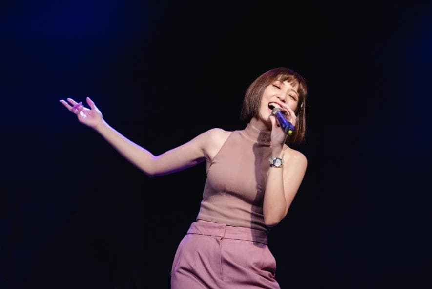 這張「一位女性歌手在舞臺上唱歌」的照片是。她穿著一件粉紅色的上衣和褲子,正在用麥克風唱歌,她的表情很投入。