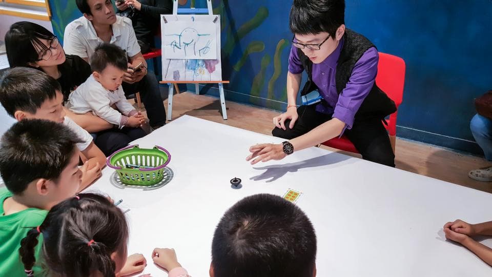 這張照片是一群人在室內玩遊戲,一位身穿紫色上衣的年輕男子正在表演魔術。