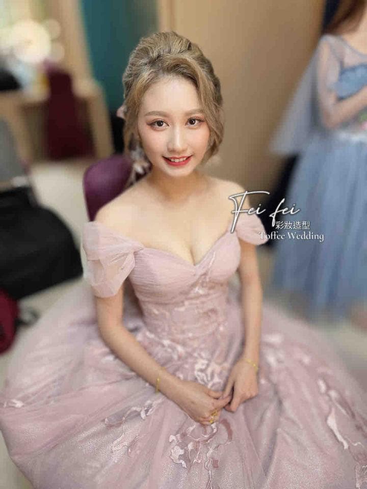 這張照片是一個穿著粉紅色婚紗的女孩。她有漂亮的臉龐,戴著優雅的耳環,正坐在椅子上。她的婚紗上有精緻的刺繡,看起來非常美麗。