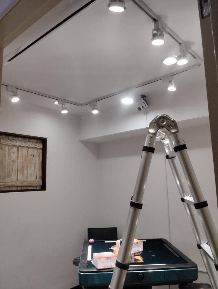 這張照片是一間房間的裝修過程,重點是裝潢師傅正在使用梯子更換天花板上的燈泡。