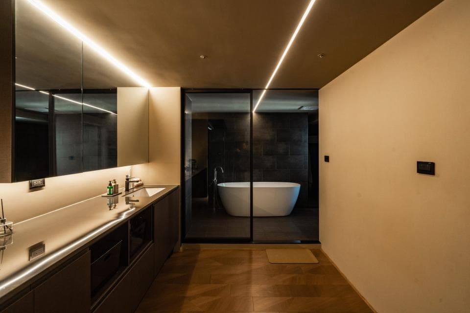 1) 照片顯示一個現代浴室,裡面有洗臉台和鏡子,浴室的牆壁和地板都是淺色系的,房間內有兩個方形的燈,浴室裡有一個黑色的浴缸