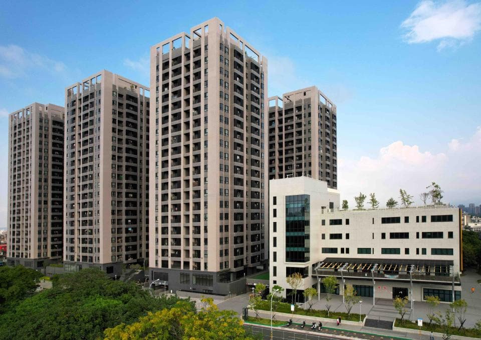 這張「公寓大樓」的照片是三棟高聳的建築,中間一棟最高,旁邊兩棟稍矮,下方有一棟低矮的建築,所有的建築都有很多窗戶和陽臺,並被綠色植物包圍。