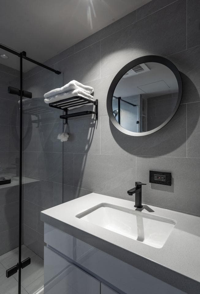 1) 照片顯示一個現代風格的浴室,配備一個白色檯面洗手台,上面有一個方形的陶瓷水槽和一個黑色水龍頭