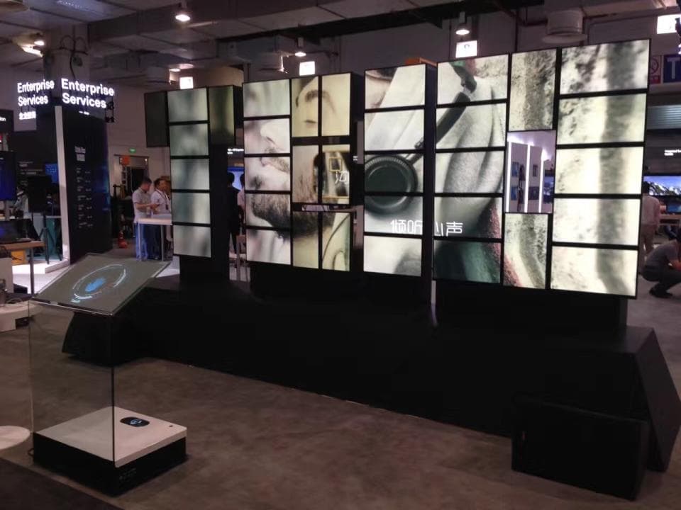 這張「展示牆」的照片是一個由多個螢幕組成的牆面,螢幕上播放著影片,牆面下方有一個透明的展示櫃。