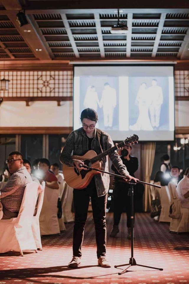 這張「婚禮現場」的照片是一個吉他手正在舞台上表演,他穿著藍色的襯衫,正在彈著一把木吉他,他的前面有一個麥克風架。