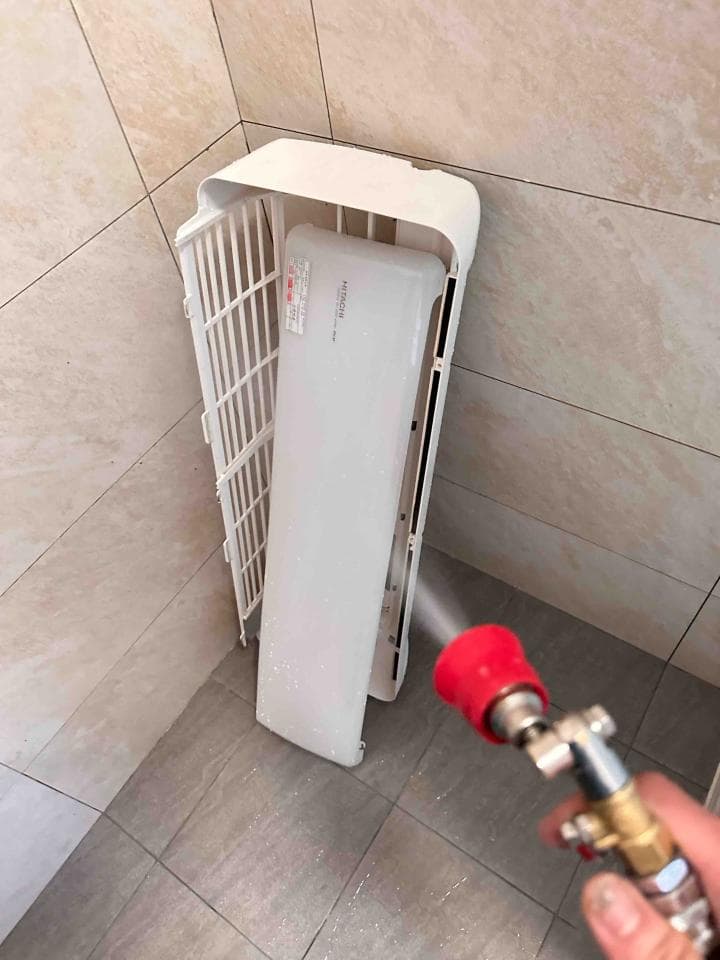 1. 照片顯示一個白色塑膠外殼的空調,空調外殼有格狀設計,並放置在浴室的牆壁上,照片右邊有一隻手拿著一個噴霧瓶