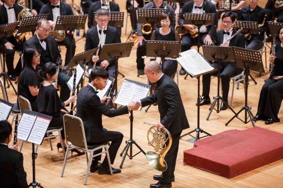 這張照片是 一位身穿西裝的男子在樂團演奏後接受另一位身穿西裝的男子的鼓勵。 他們彼此微笑,看起來很開心。