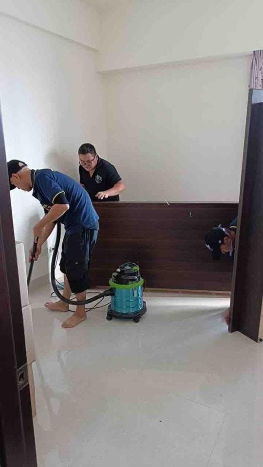 這張照片是一間房間正在裝修,一個穿著黑色衣服的男人站在房間的右側,他拿著工具正在修理房間的牆壁,另一個穿著藍色衣服的男人在房間的左側,他正在用吸塵器清理房間的地板。