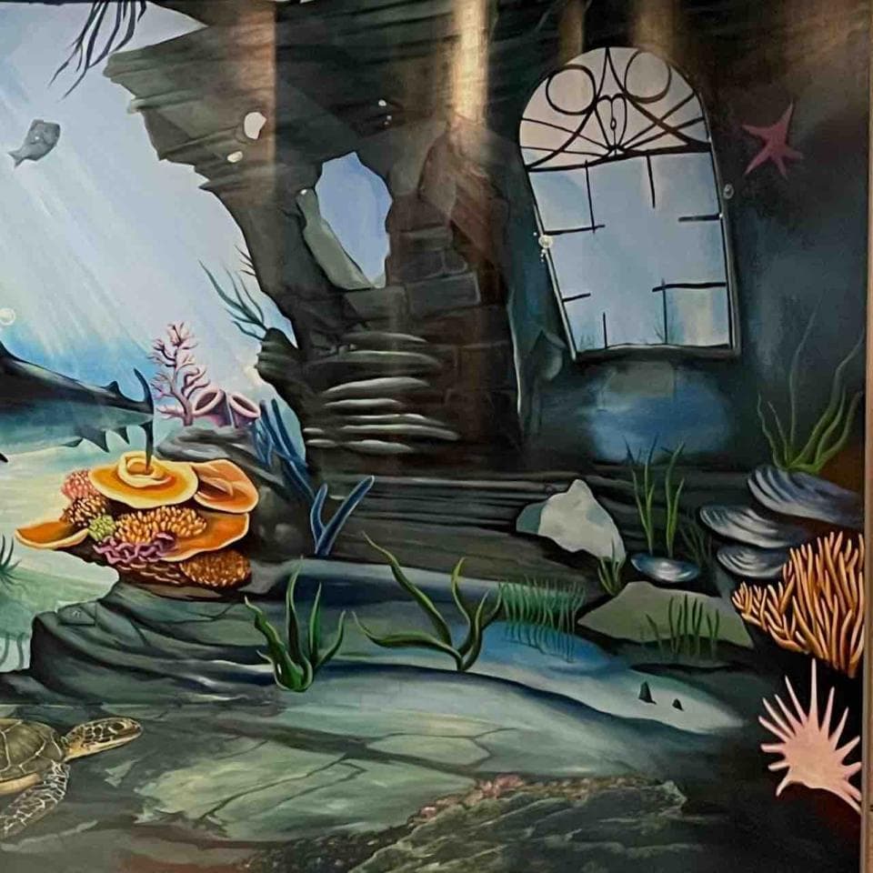 這張照片是一幅海邊的壁畫,畫中有一扇窗戶,窗戶上有精緻的雕花,窗戶後面的景色被黑暗籠罩,營造出一種神秘感。