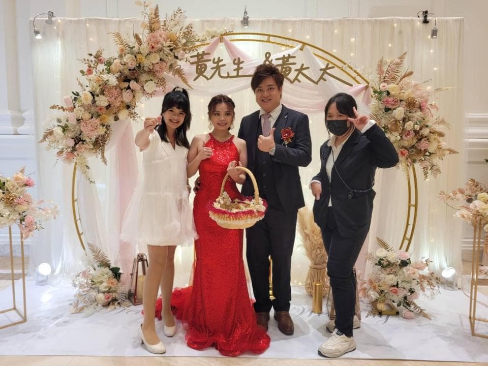 這張照片是婚禮現場,新郎新娘站在花拱門下,背景是佈置精美的婚禮場地。