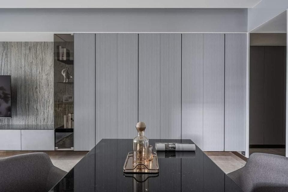 這張照片是展示一個現代化的餐桌,桌面上擺放著一個金色的裝飾品和一個黑色的託盤,背景是一面帶有垂直線條的白色牆壁。