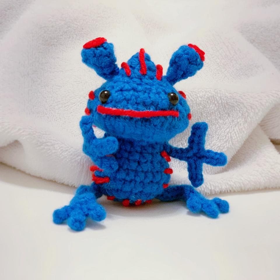 這張「毛絨玩具」的照片是一個藍色的毛絨玩具,有著紅色和黑色的細節,它看起來很可愛。