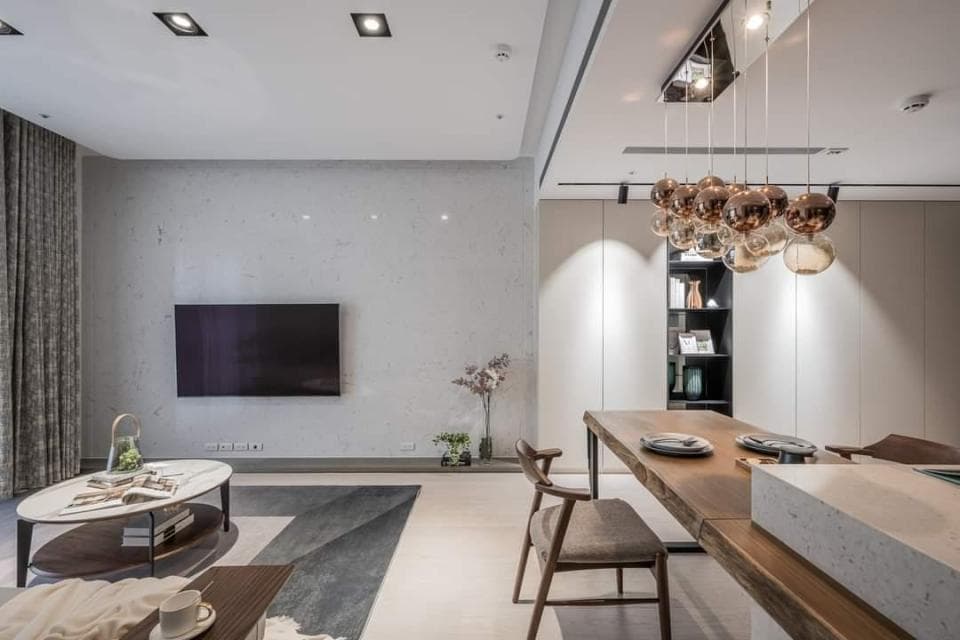 這張「現代簡約風格客廳」的照片是一間寬敞的客廳,佈置簡潔,牆壁是淺灰色,搭配木製地板和沙發。客廳裡有一臺電視,以及一張咖啡桌,還有幾盆綠色植物。客廳的另一邊是餐桌,餐桌旁有一張木椅。