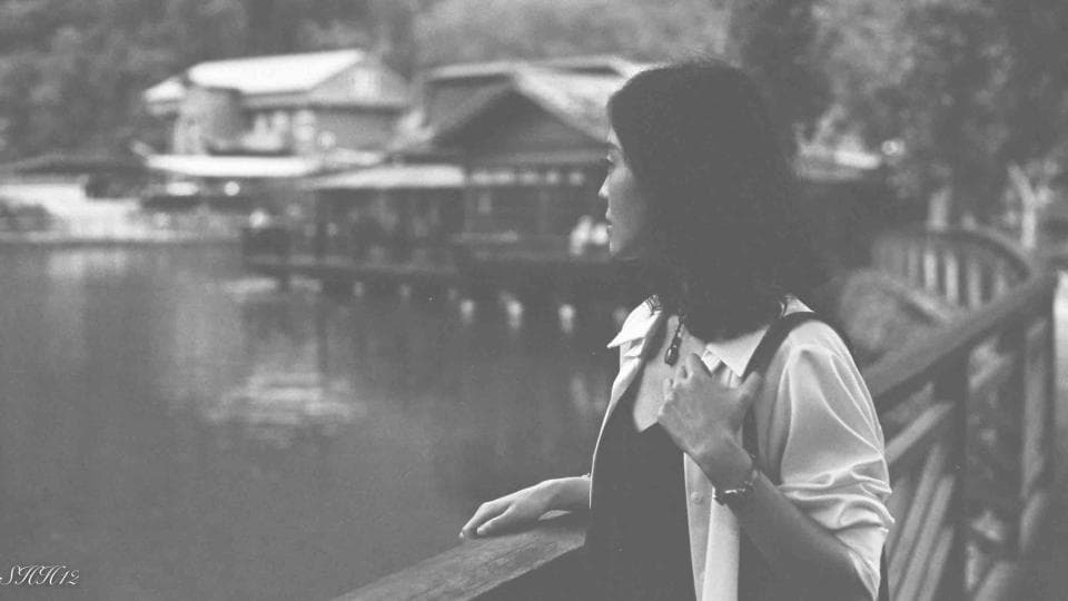 這張照片是一名女子站在橋上,背景是湖泊和建築。