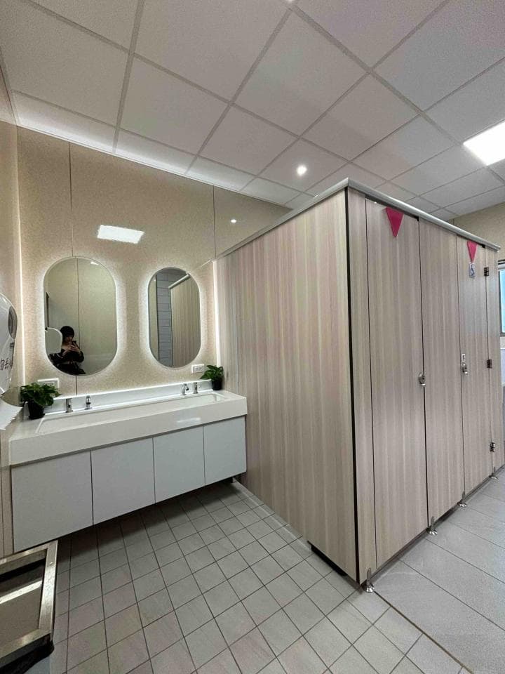 1) 照片顯示一個帶有兩個洗手台和鏡子的現代化公共洗手間,牆上安裝了木製隔板,地板鋪著瓷磚