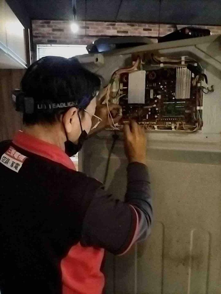 1) 照片中有一名身穿紅黑相間上衣的男子,正低頭修理牆上的電路板