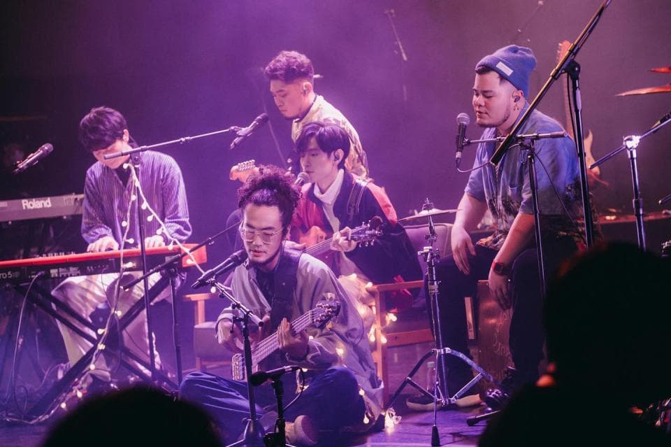 這張照片是一群人在舞臺上表演,最重要的是在舞臺中央的吉他手,他正在彈奏一把電吉他,他的表情專注,動作靈活,讓觀眾感受到音樂的活力。