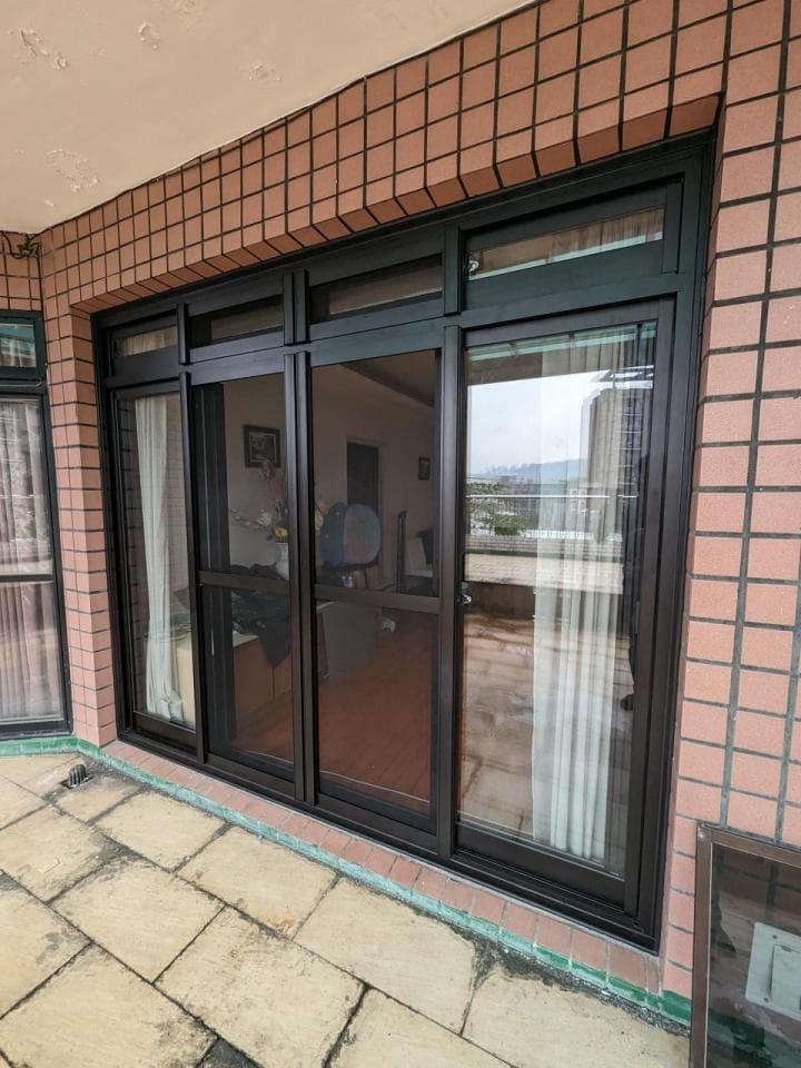 這張照片是現代化的建築物,擁有大型落地窗,並以棕色磚塊裝飾牆面。窗戶採用黑色鋁框,並搭配網紗,可提供防護和通風效果。