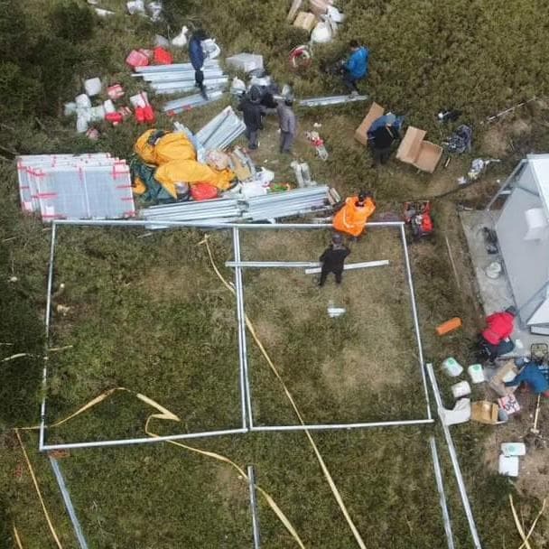 1) 照片顯示一組人在草地上,他們正在搭建一個金屬框架結構