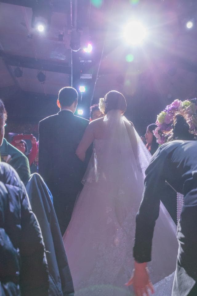 這張「婚禮」的照片是一對新人,新郎穿著西裝,新娘穿著白色婚紗,他們正在步入會場,周圍有許多賓客。