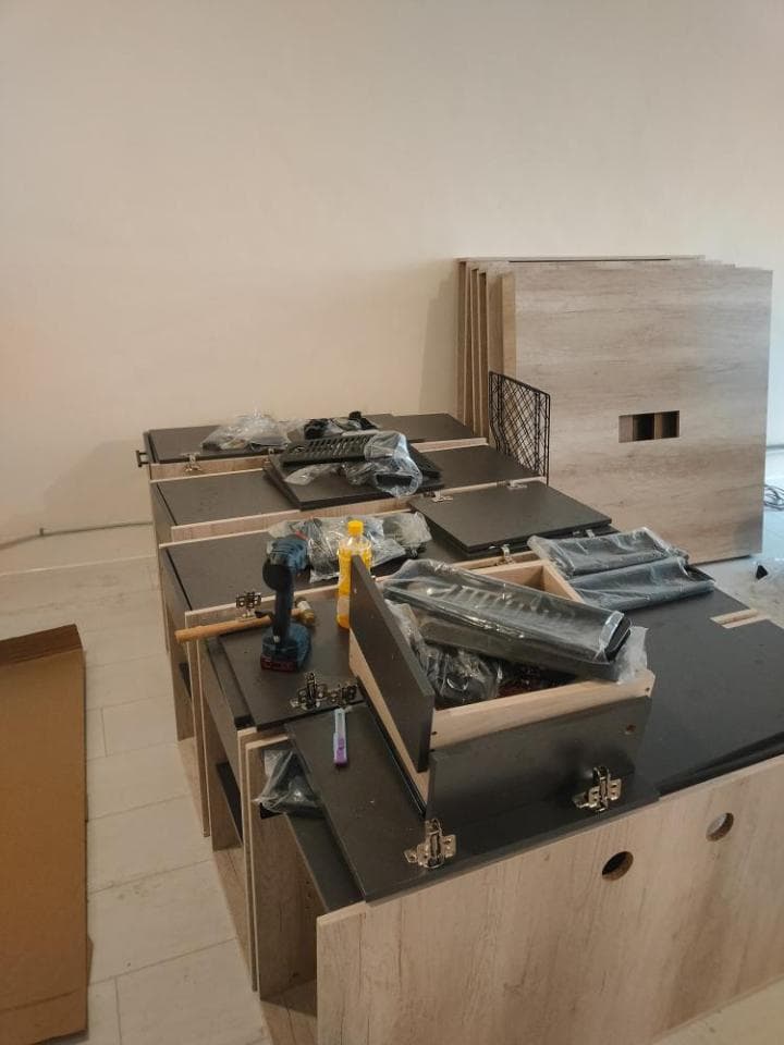 這張照片是一堆組裝好的木質家具,其中最顯眼的是一個正在組裝中的木製抽屜櫃,它有幾個抽屜,並配備了黑色五金配件,其中一個抽屜還放著一個黃色的工具盒。